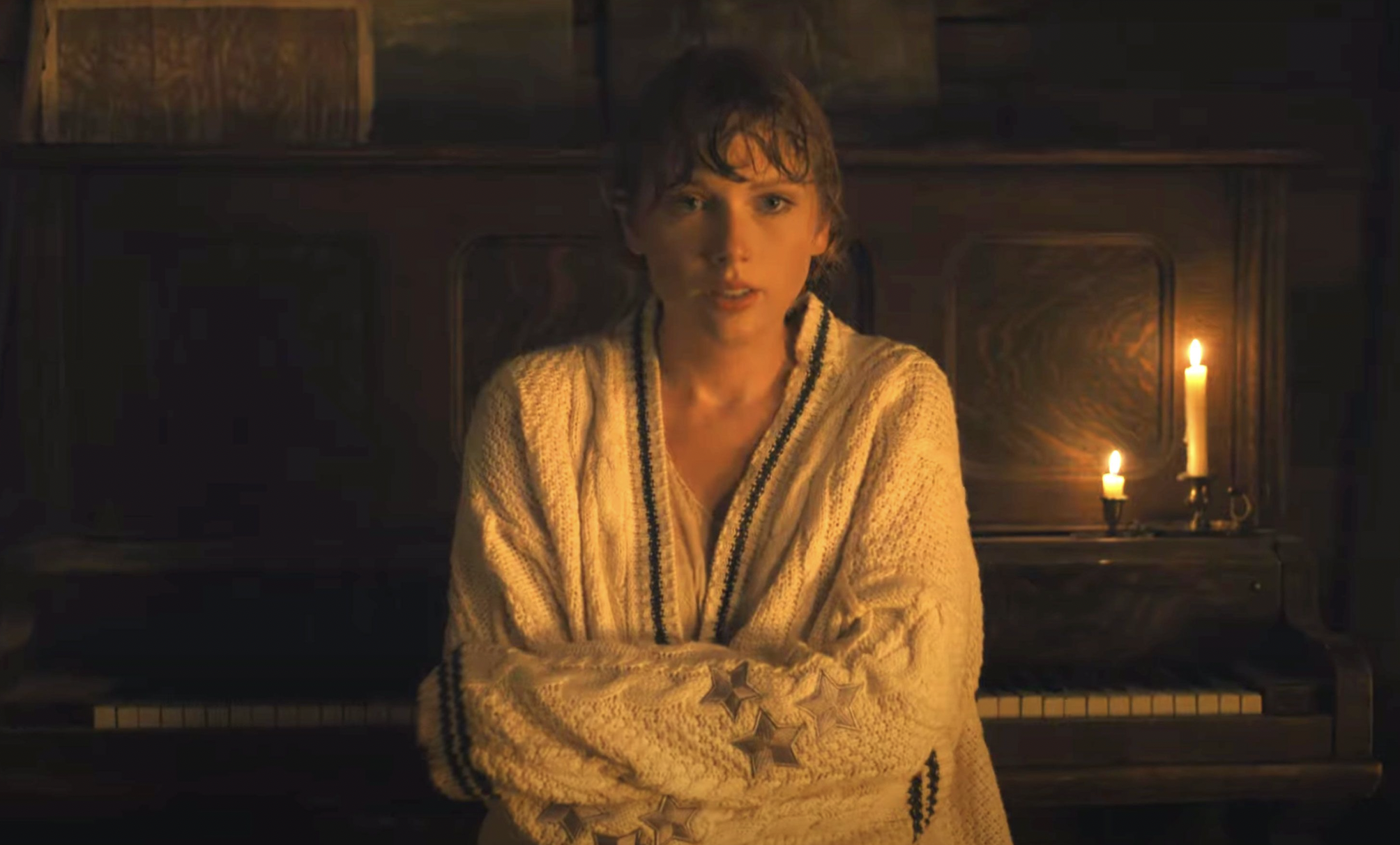 Taylor Swift in front of a fireplace wearing a large cardigan, which can easily be a folklore costume